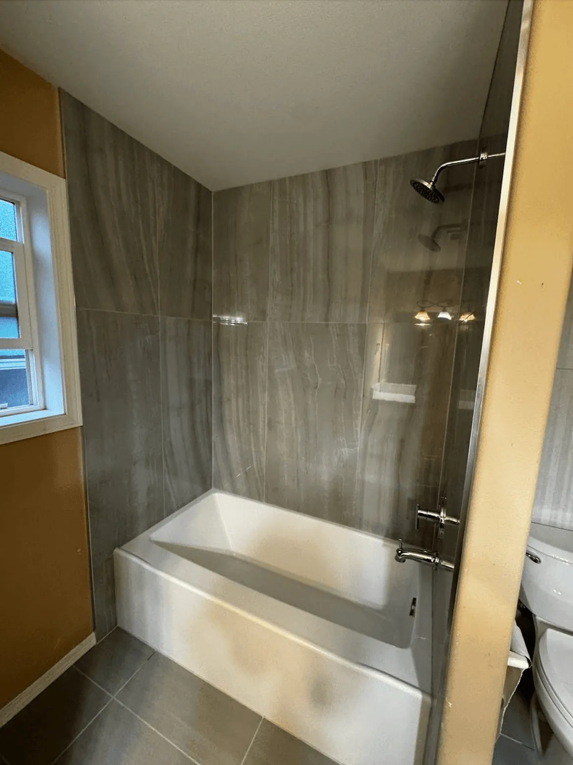Large gray veined tile tub surround up to the ceiling, with a glass shower panel